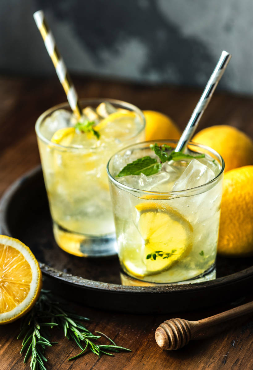 Two glasses of lemonade with lemons, ice, mint, and straws.